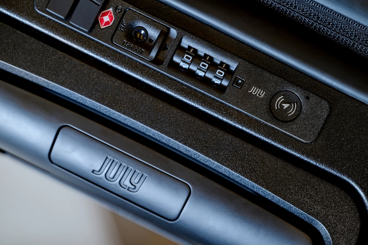 Close-up detail of the Qantas × July suitcase's TSA lock system, showing the integrated CaseSafe tracking technology