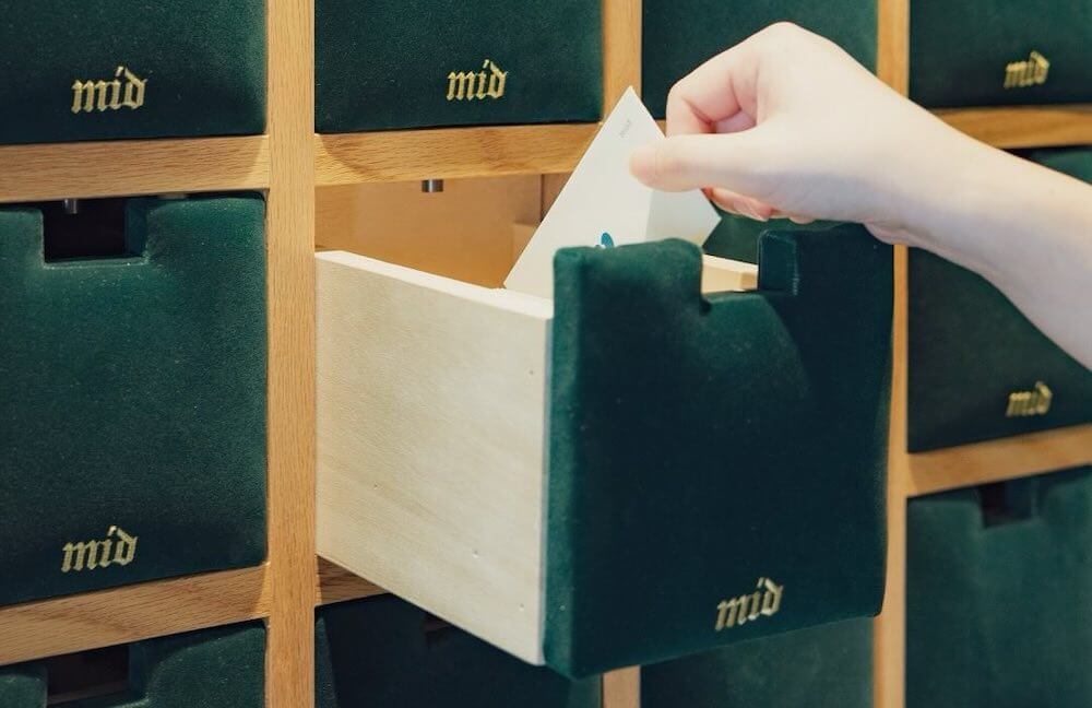 Green velvet cubby drawers marked 'mid', with a hand pulling an envelope from one