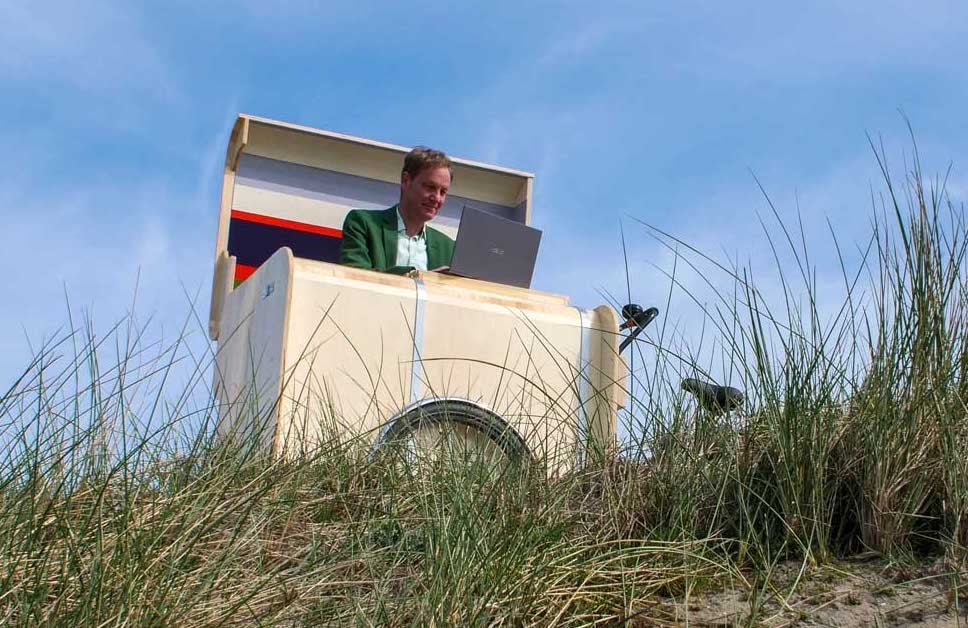 Man working on a laptop inside a bicycle office parked at the beach