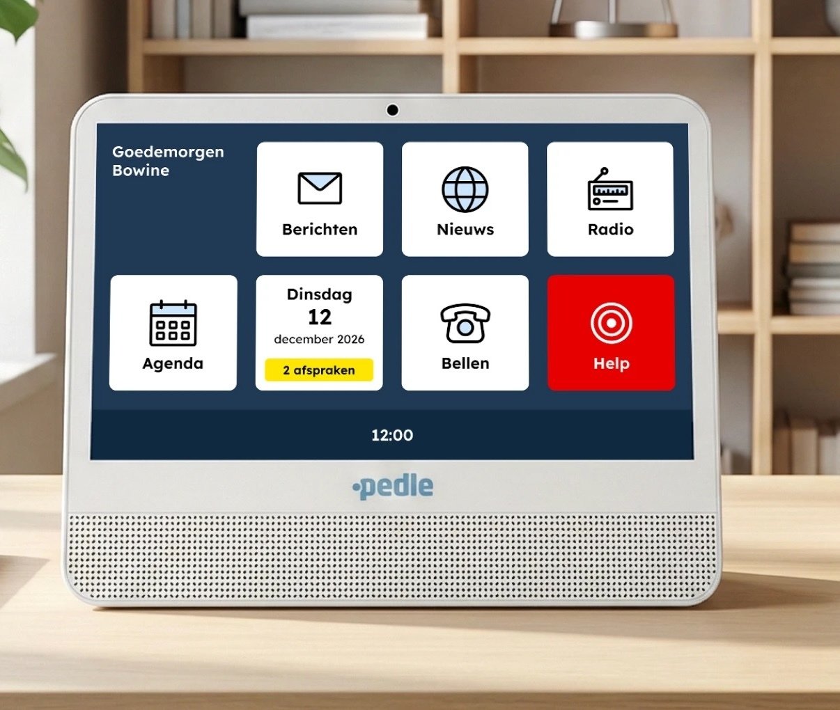 A Pedle computer on a wooden surface displaying its home screen with large icons for messages, news, radio, agenda, calling and a red help button, greeting the user by name