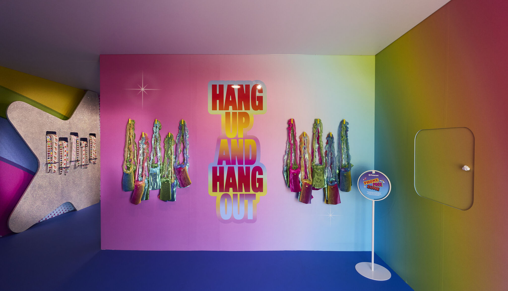 A rainbow-gradient wall inside the Pinterest activation displays the phrase "HANG UP AND HANG OUT" in large block letters, flanked by bedazzled Yonder phone pouches