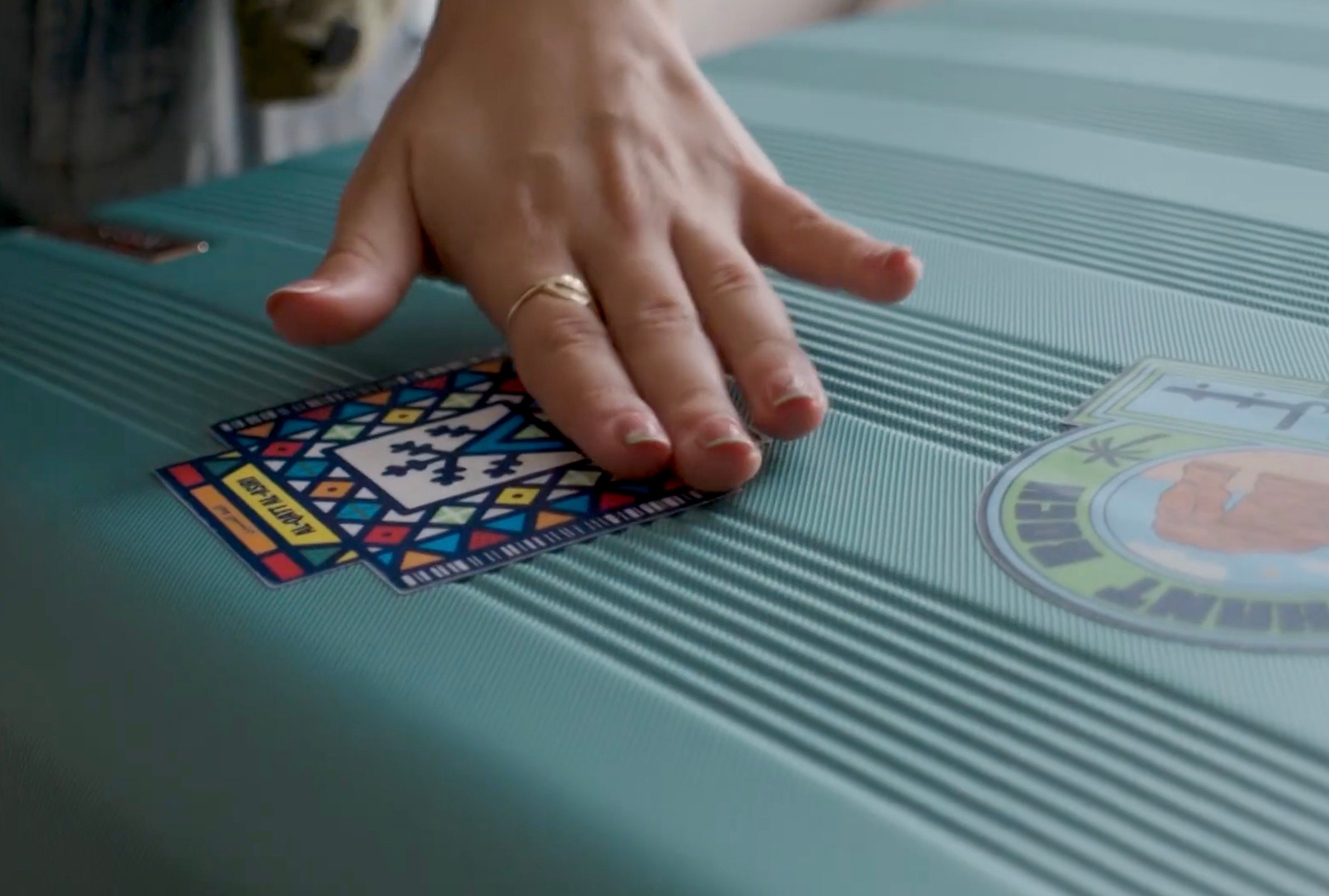 Traveler's hand placing a colourful geometric patterned sticker on teal luggage as part of Saudia's Let It Fly program