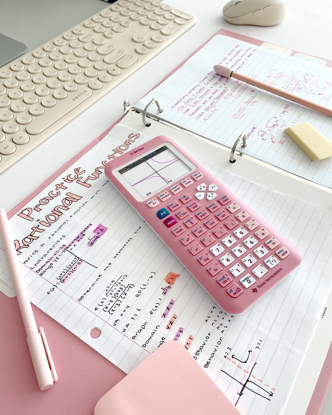 Pink TI-84 Evo graphing calculator displaying a rational function graph, resting on a handwritten math worksheet titled 