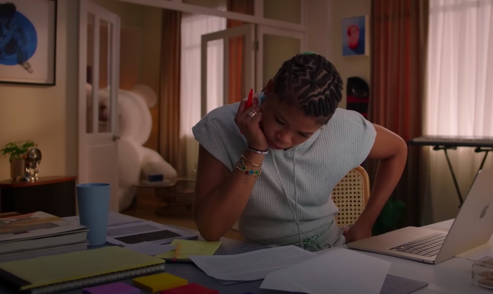 Storm Reid at desk, looking down at documents with chin resting on hand