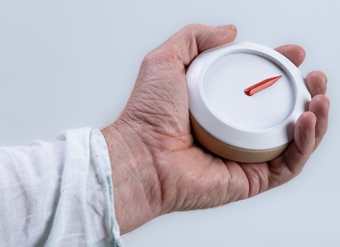 A hand holding Het Kompas, a small round navigation device with a single red pointer for guiding people with dementia safely home 