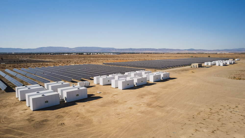 In a desert landscape, rows of white battery containers and solar panels