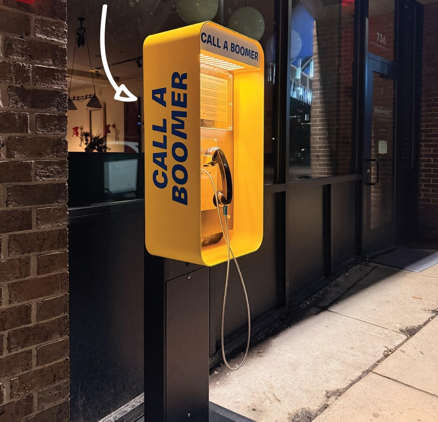 A bright yellow payphone kiosk mounted on a black metal post on a city sidewalk, with 
