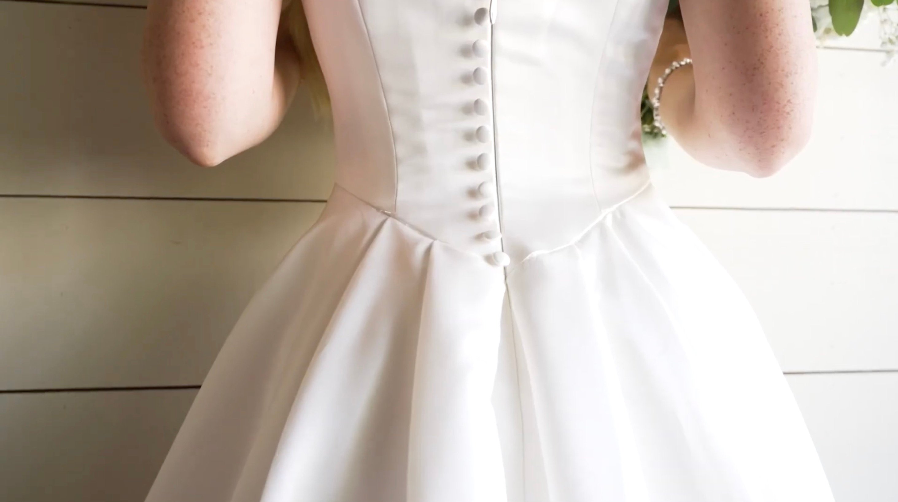Close-up of a bride's torso in a white satin wedding gown with a row of fabric-covered buttons down the back 