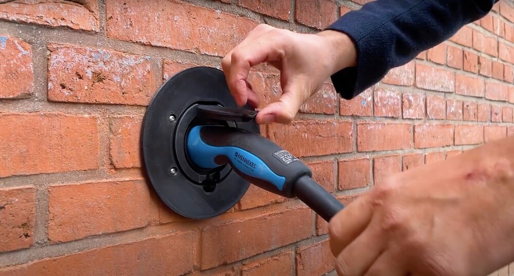 Hands removing charging cable from an Elby socket on a building's exterior wall