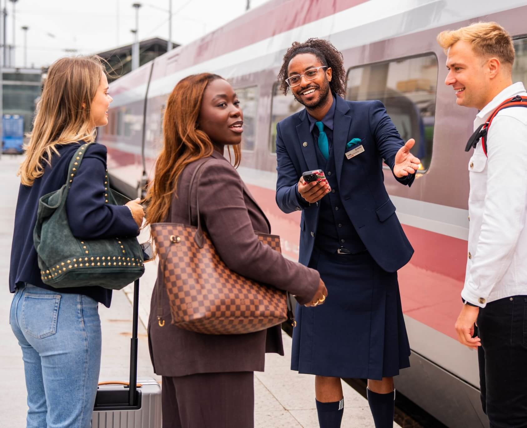 Eurostar employee in navy blazer and knee-length skirt greets passengers on platform beside train 