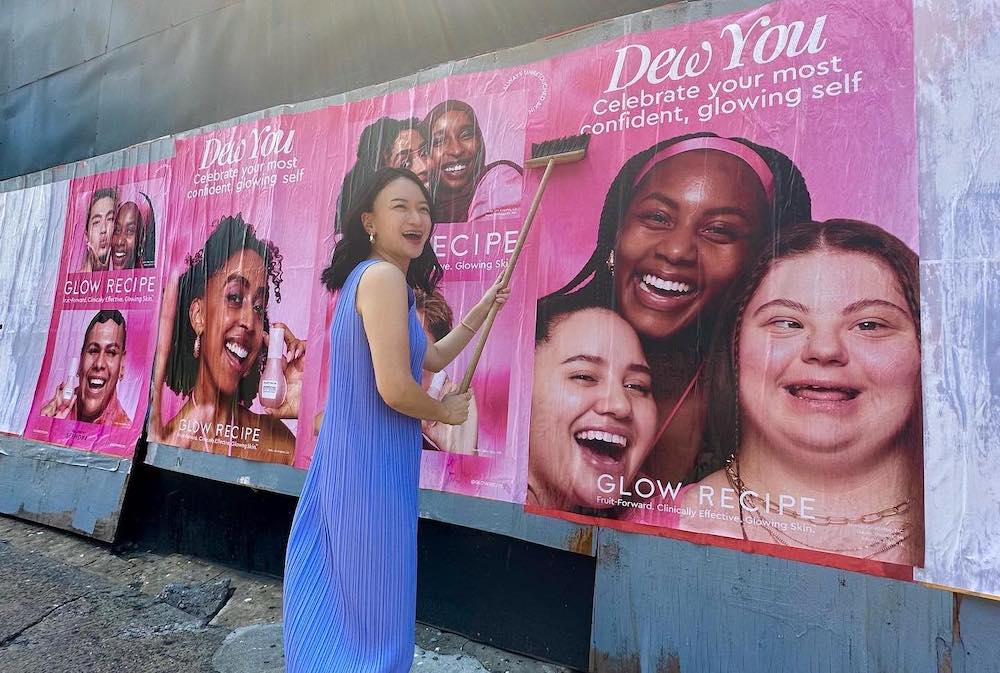 Glow Recipe's co-CEO Christine Chang wheat-pastes a Dew You campaign poster onto a wall