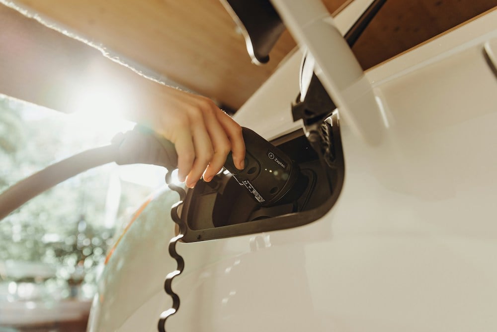 Hand inserting a charger plug into an EV, with sun flare in the background