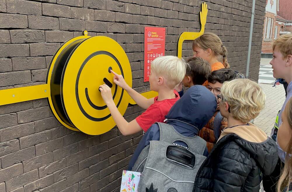 Kids crowded around a Happy Speeltijd wheel mounted on a wall