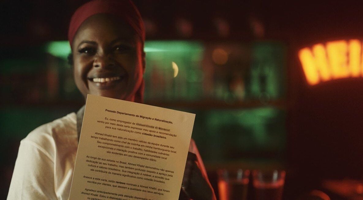 Woman in kitchen uniform, smiling and holding a letter from the Brazilian government 