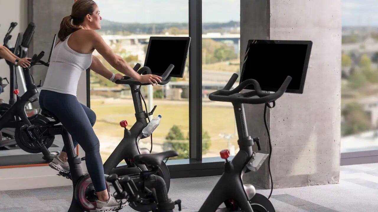 Hotel guest working out on a Peloton bike in a fitness center with an expansive view 