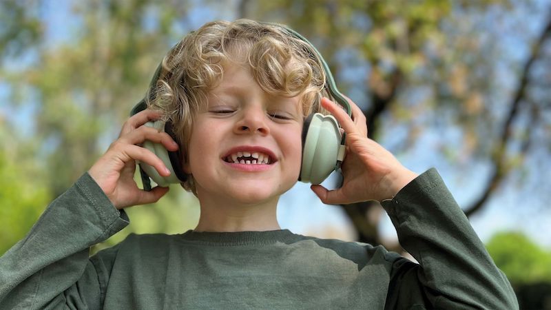 Child with curly blond hair and light green, over-ear headphones