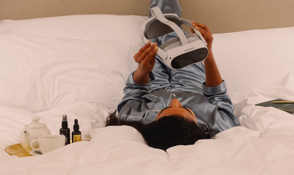 Woman in blue satin pajamas holding a VR headset