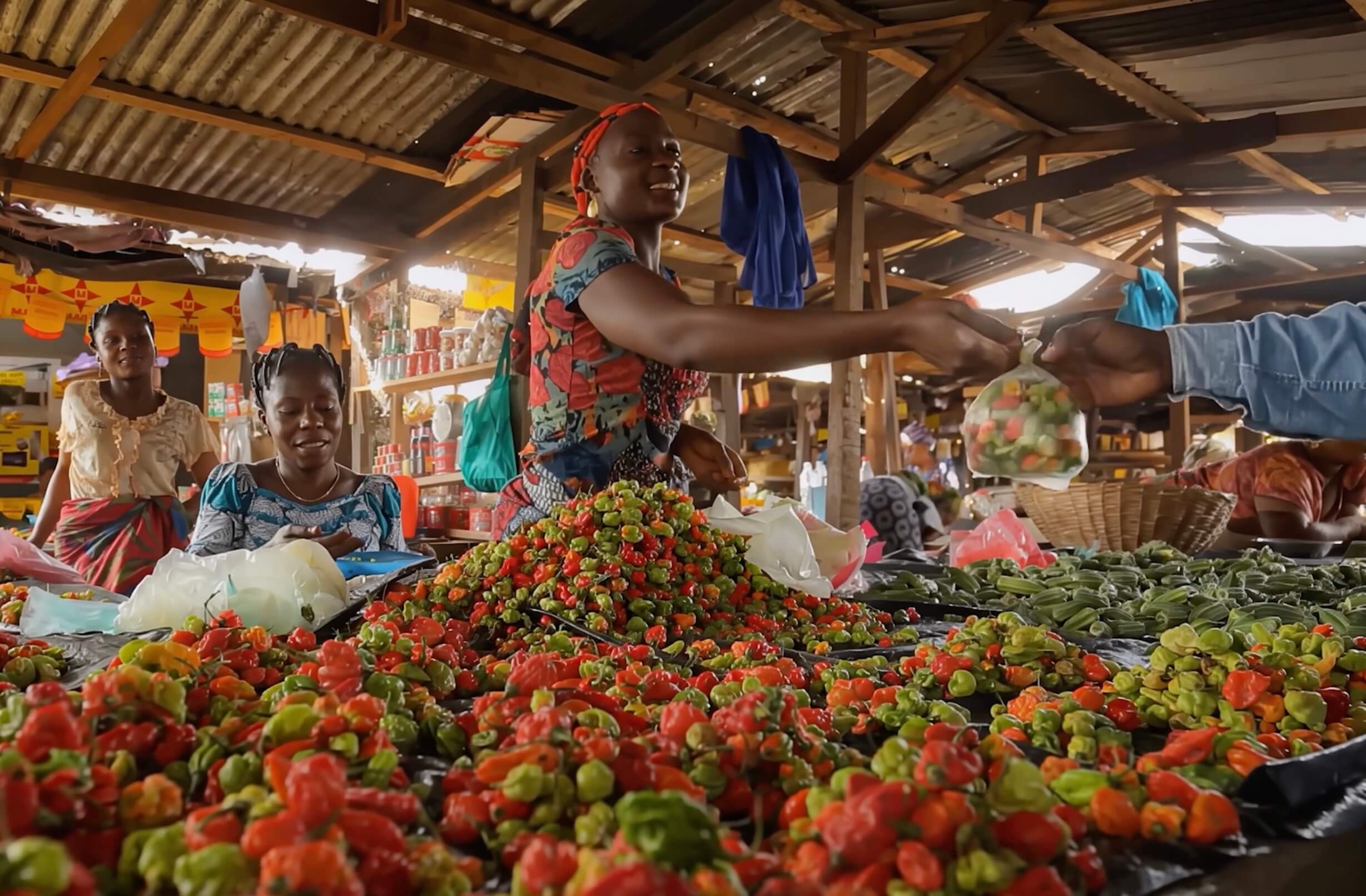 Women selling colorful fresh peppers and vegetables at an open-air market stall under a corrugated metal roof in West Africa 