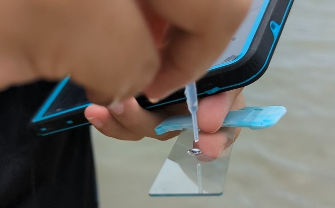 One hand dropping liquid onto glass plate, other holding phone