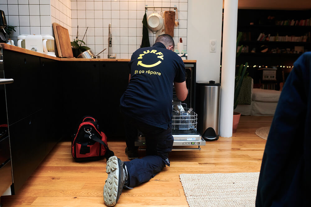 Technician in a Murfy shirt working on a dishwasher in a home kitchen
