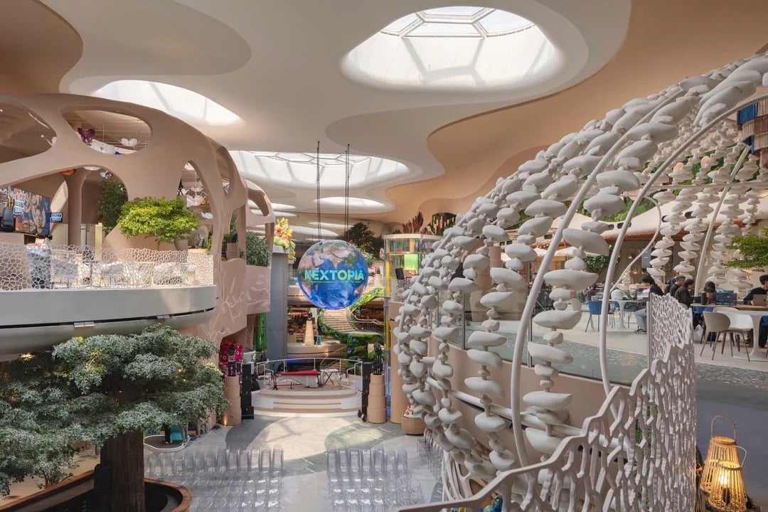 Interior view of NEXTOPIA at Siam Paragon featuring a large suspended LED globe, organic curved architecture, lush indoor trees, sculptural installations made of white stacked forms and open seating areas 
