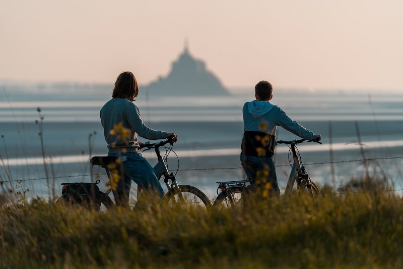 Two cyclists pausing to enjoy a sunset view of Mont-Saint-Michel