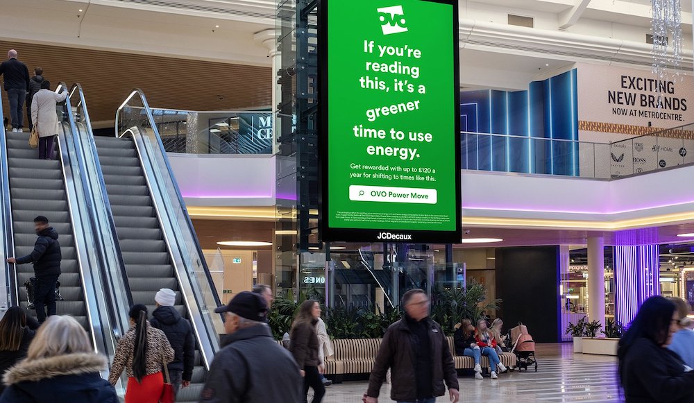 Digital display in shopping mall. Text: 'If you're reading this, it's a greener time to use energy'