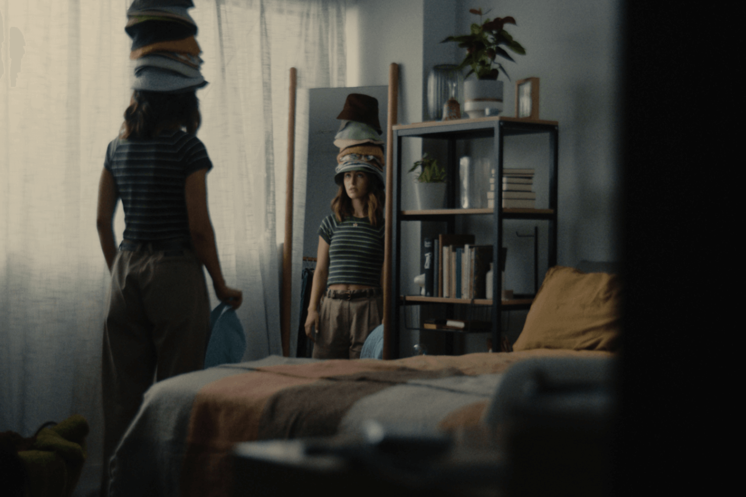 Female-presenting person looking in the mirror, wearing a stack of bucket hats 