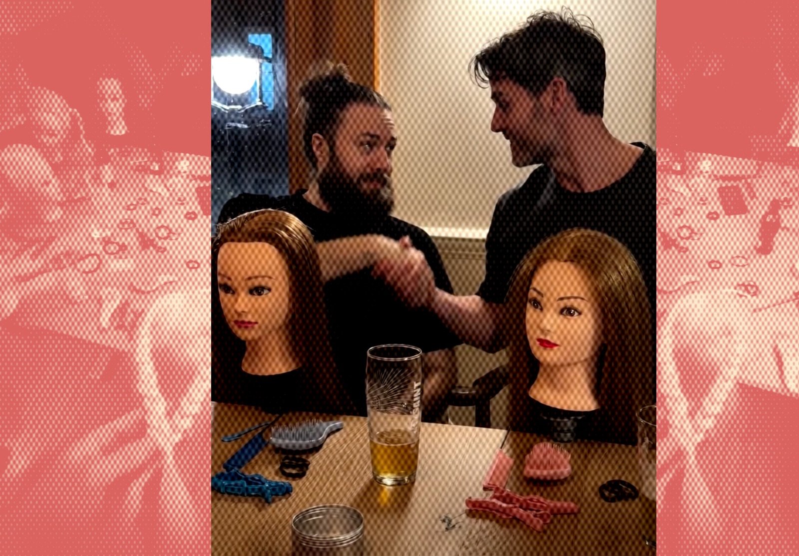 Two men practice braiding techniques on hair mannequins at a pub table scattered with clips, brushes and hair ties, a glass of beer in the foreground 