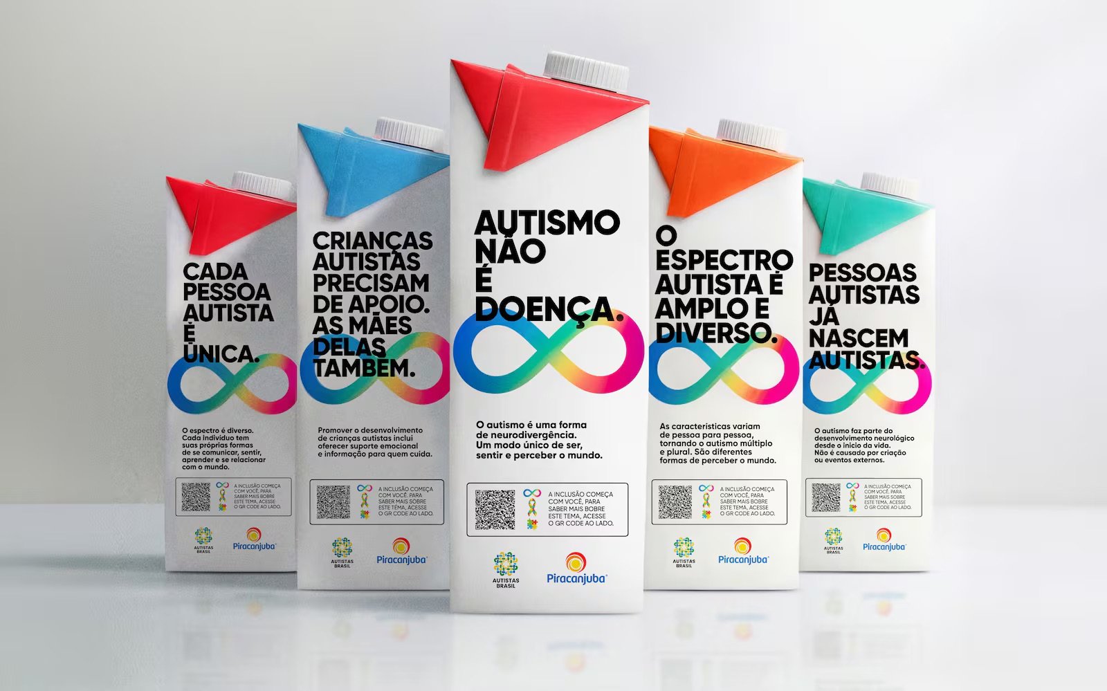 Five Piracanjuba UHT milk cartons in a row, each with a different colored top and a bold Portuguese headline about autism above a rainbow infinity symbol and a QR code 
