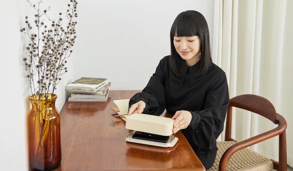 Marie Kondo at a desk, placing a phone in a Stolp phone box 