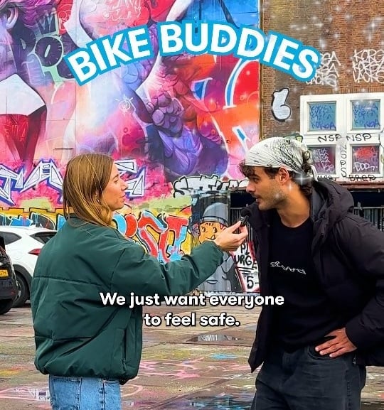 Two young people stand chatting and smiling outside the DGTL festival venue in Amsterdam, with vibrant graffiti murals behind them. One wears a green Swapfiets crew jacket. Text overlay reads 