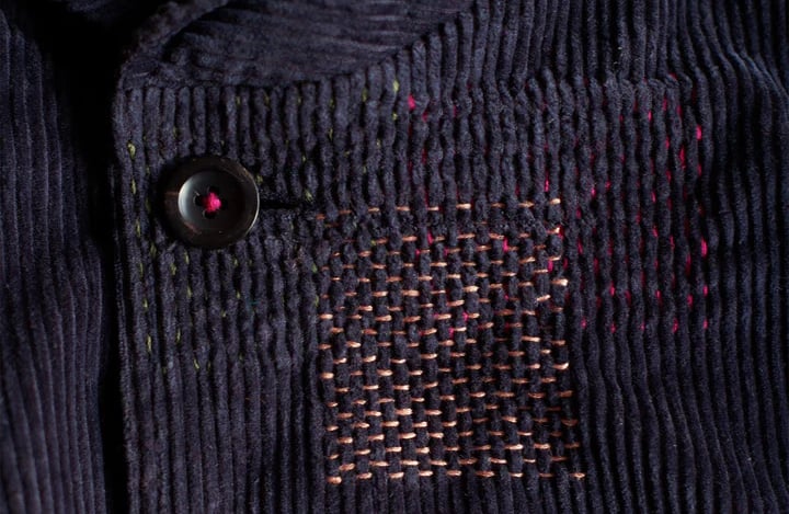 Visible mending on a dark blue corduroy jacket, in contrasting stitching