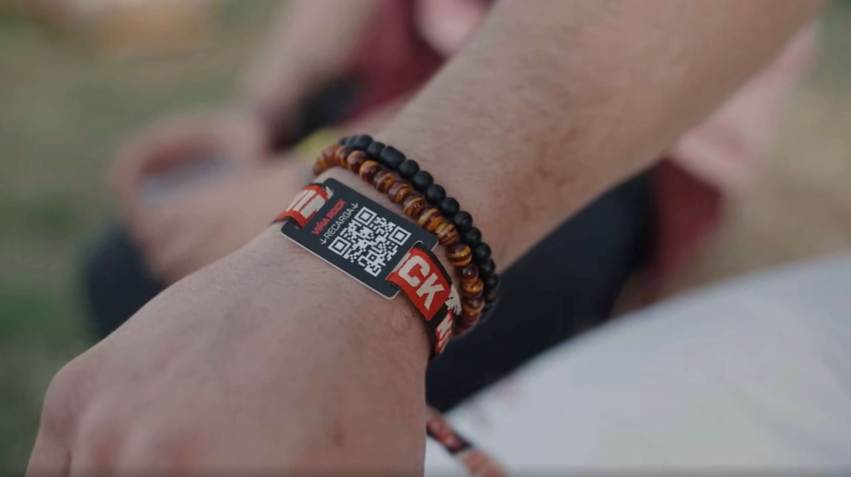 Close-up of a person's wrist wearing a Viña Rock festival cashless wristband with a QR code for top-ups, layered with two beaded bracelets 