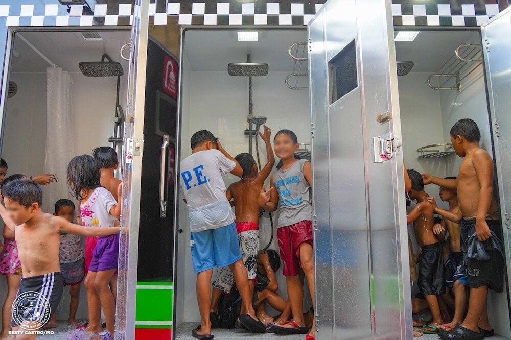 Kids dressed in summer clothing, playing around in mobile showers 