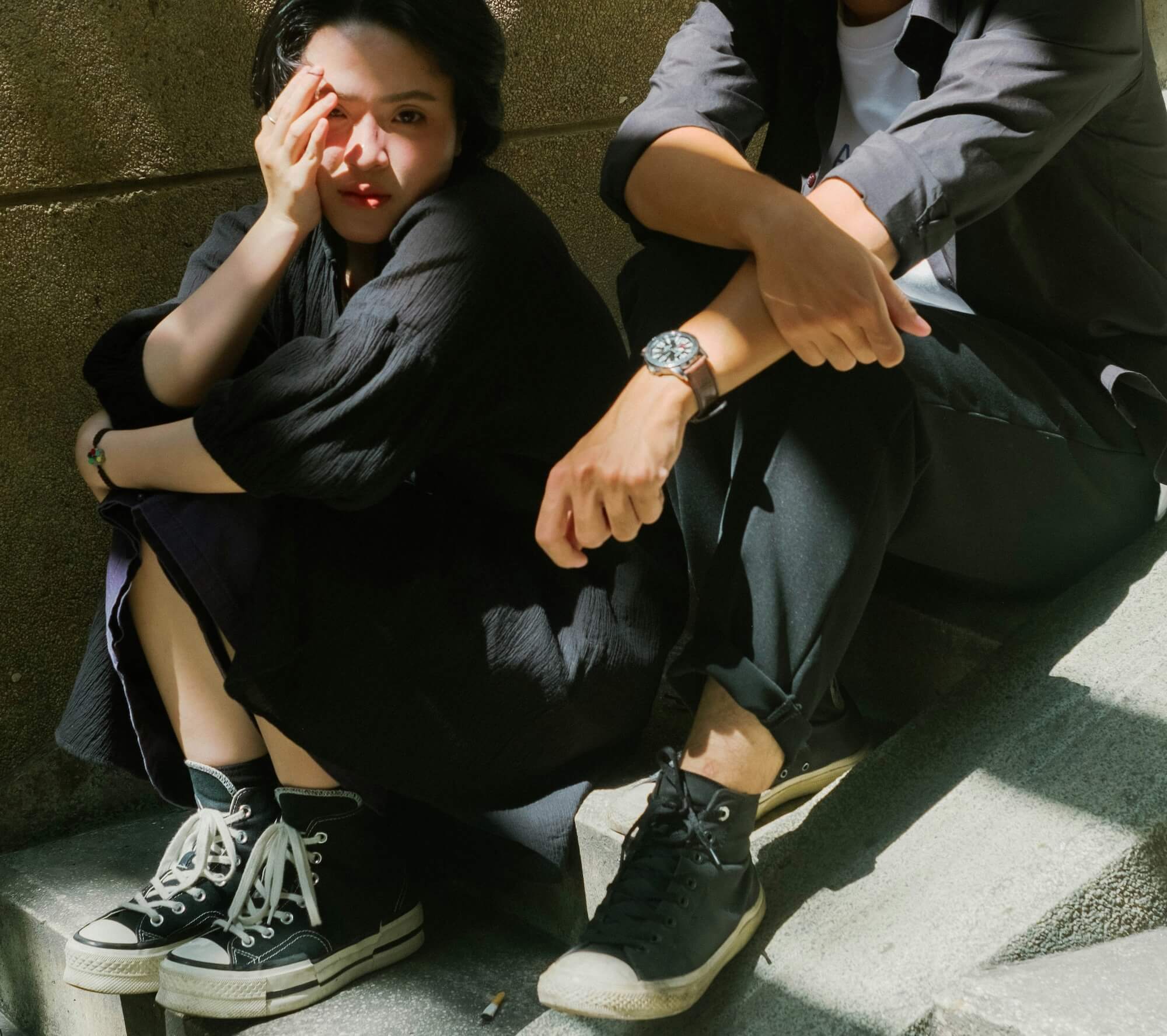 Two young people sitting on outdoor steps in sunlight, one resting their face in their hand, both looking away from each other 