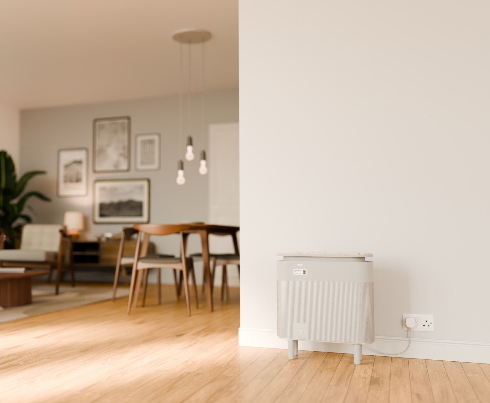 A compact, light grey home battery with ribbed front panel and short legs, plugged into a standard wall socket in a modern apartment with wooden floors and mid-century furniture visible in the background 